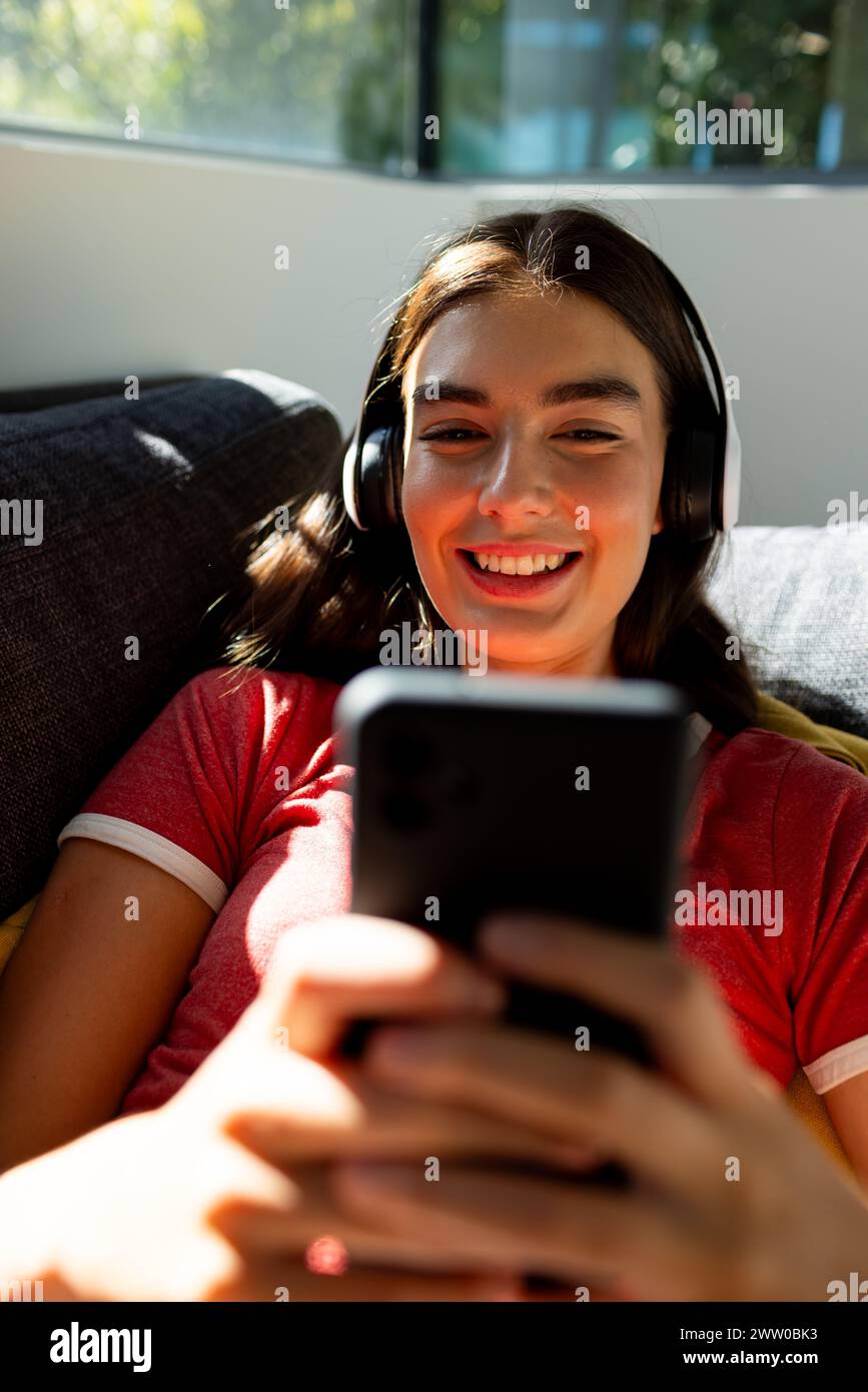 Eine junge weiße Brünette macht sich mit ihrem Smartphone zu Hause auf der Couch auf Stockfoto