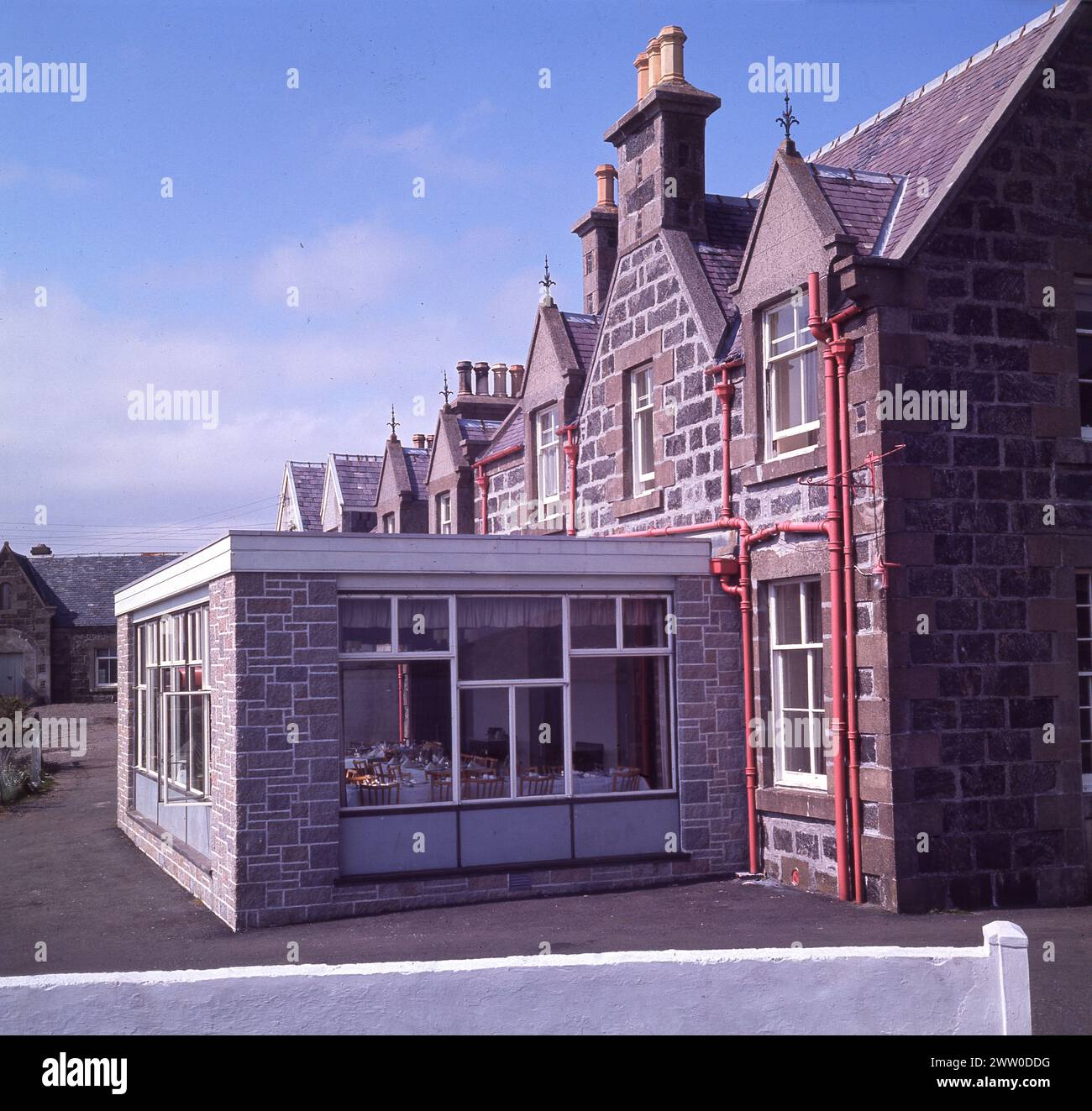 1960er Jahre, historisch, Blick auf die hintere Erweiterung des Lochboisdale Hotels auf der Isle of South Uist, Western Isles, Schottland, Großbritannien. Der 'moderne' einstöckige Anbau wird als Speisesaal genutzt. Das Hotel stammt aus den 1880er Jahren und die Eigentümerin des Anwesens, Lady Gordon Cathcart. Stockfoto