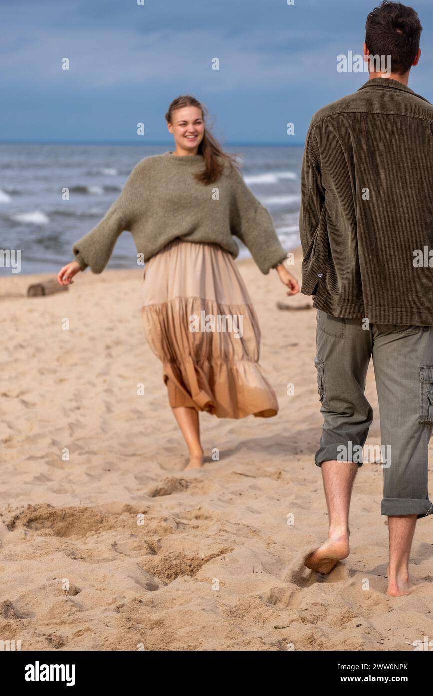 Ein Paar, das am Strand spaziert, eine Frau in beigem Rock und grünem Pullover, ein Mann in einem olivfarbenen Hemd. Stimmung für unbeschwerte Freizeit, geeignet für Reisen oder romantische Themen Stockfoto