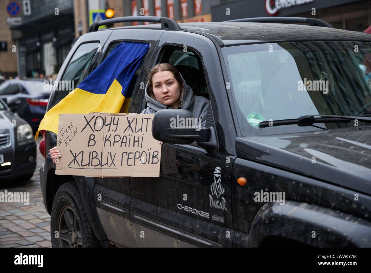 Der ukrainische Patriot zeigt aus dem Fenster eines fahrenden Autos das Banner „Ich will im Land der lebendigen Helden leben“. Kiew - 17. März 2024 Stockfoto
