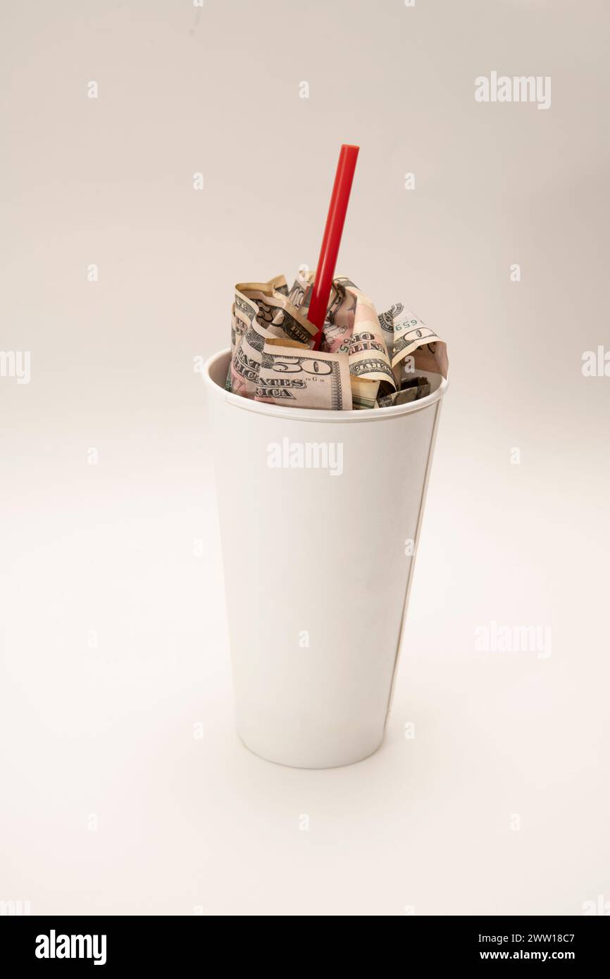 Fastfood-Konzept, das die steigenden Preise für Fastfood veranschaulicht. Soda-Becher mit Geld und einem Strohhalm auf weißem Hintergrund. Stockfoto