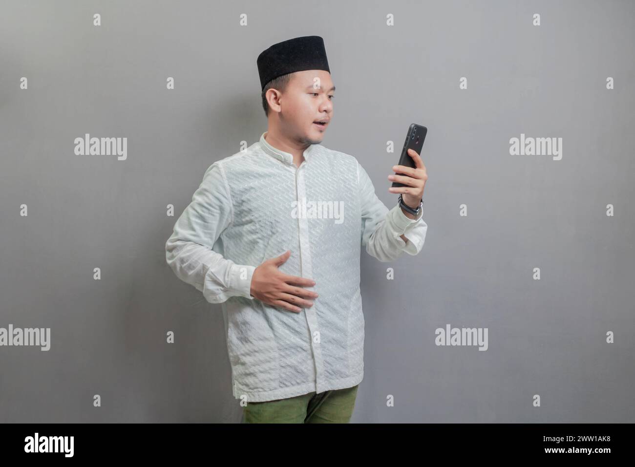 Asiatischer muslimischer Mann mit koko-Hemd und Peki in den Farben des Fastenmonats, der den Hunger zurückhält und auf die Zeit wartet, das Fasten zu brechen, isola Stockfoto