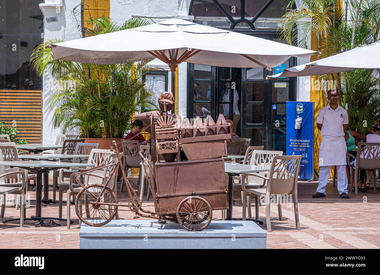 Cartagena, Kolumbien - 25. Juli 2023: Plaza de San Pedro Claver, Platz. Rostiges Metallartowork präsentiert Straßenverkäufer mit Dreirad. Restaurant mit Stockfoto