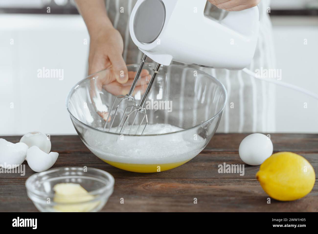 Frau Hand rührt mit Eiern weiß mit elektrischem Mixer in der Glasschale, Backrezept, Küchenhintergrund Stockfoto