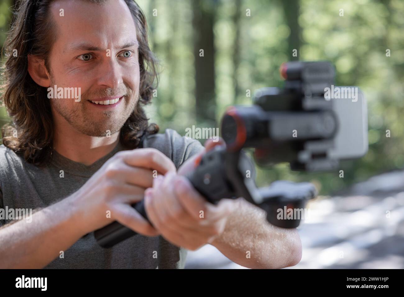 Content Creator verwendet. Ein Handy-Gimbal zum Filmen in der Natur mit einem verschwommenen Wald im Hintergrund Stockfoto