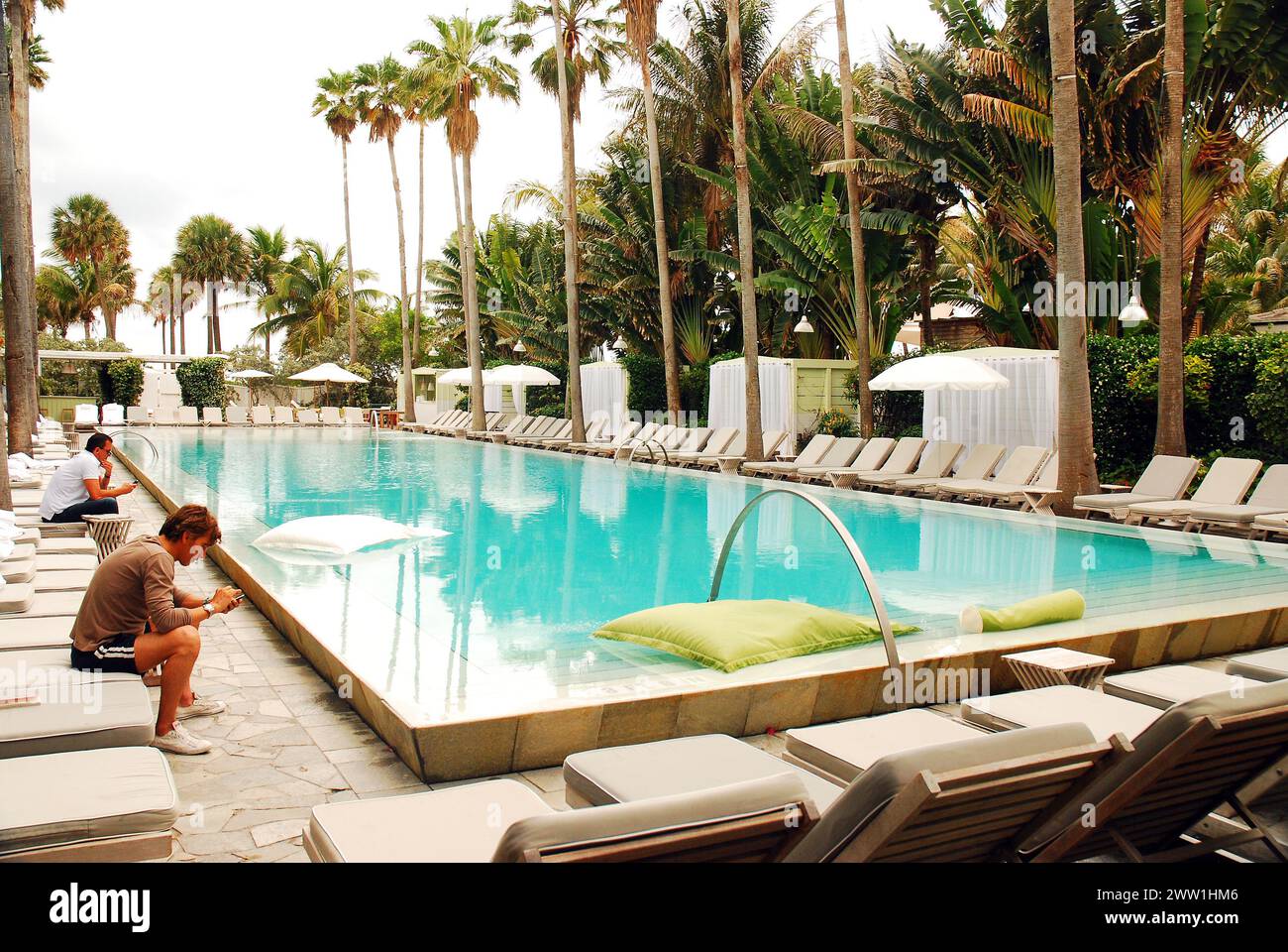 Ein junger Mann ruht in einem von Palmen umgebenen Außenpool in Miami Beach, Florida Stockfoto