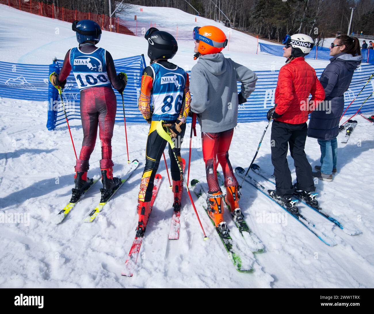 Massachusetts Interscholastic Athletic Association (MIAA) 2024 High School Alpine Skisport jährlich State Championship Slalom und Giant Slalom im Wachusett Mountain Skigebiet in Princeton, MA. Wettkämpfer Jungen und Eltern beobachten Rennen am Ende des Kurses. Stockfoto