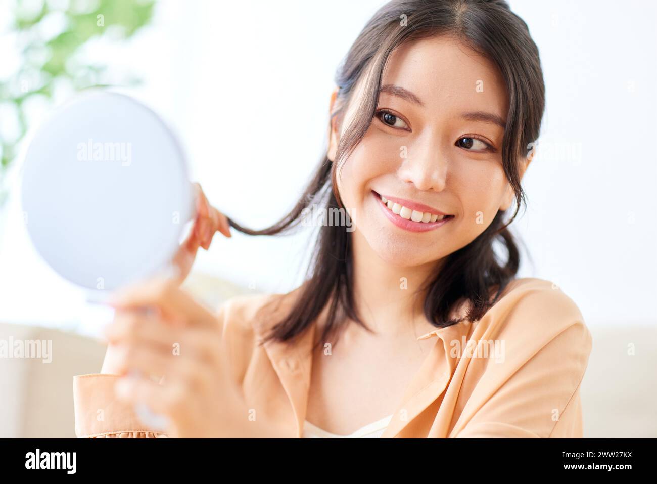 Asiatische Frau lächelt, während sie einen Spiegel hält Stockfoto