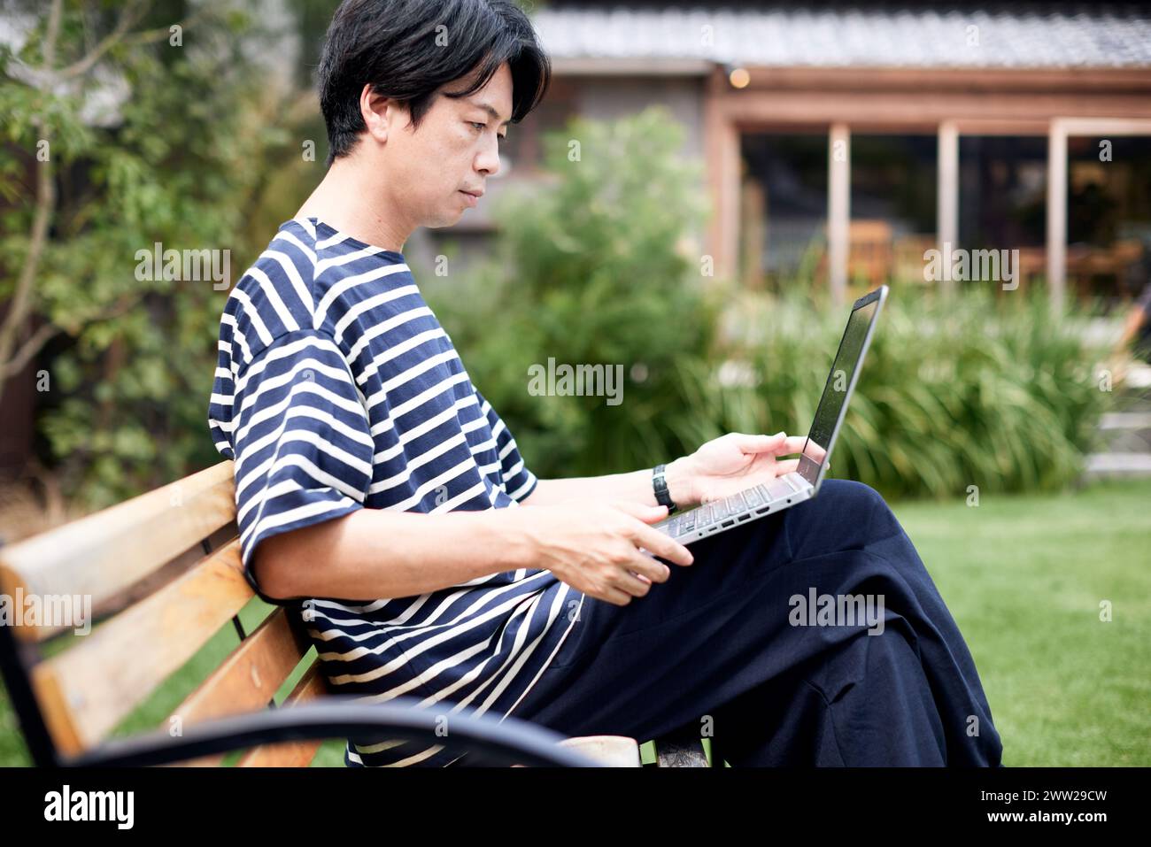 Ein Mann, der auf einer Bank sitzt und einen Laptop benutzt Stockfoto
