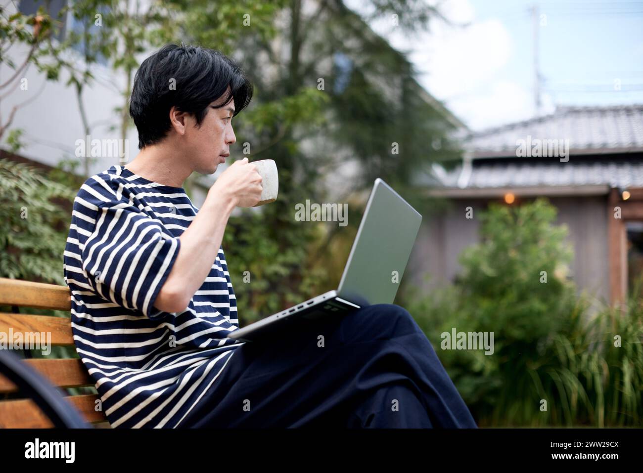 Ein Mann, der auf einer Bank mit einem Laptop sitzt Stockfoto