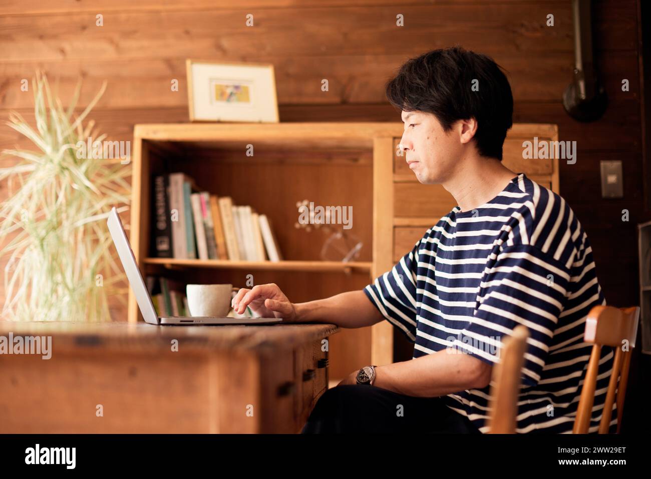Ein Mann in gestreiftem Hemd, der mit einem Laptop an einem Tisch sitzt Stockfoto