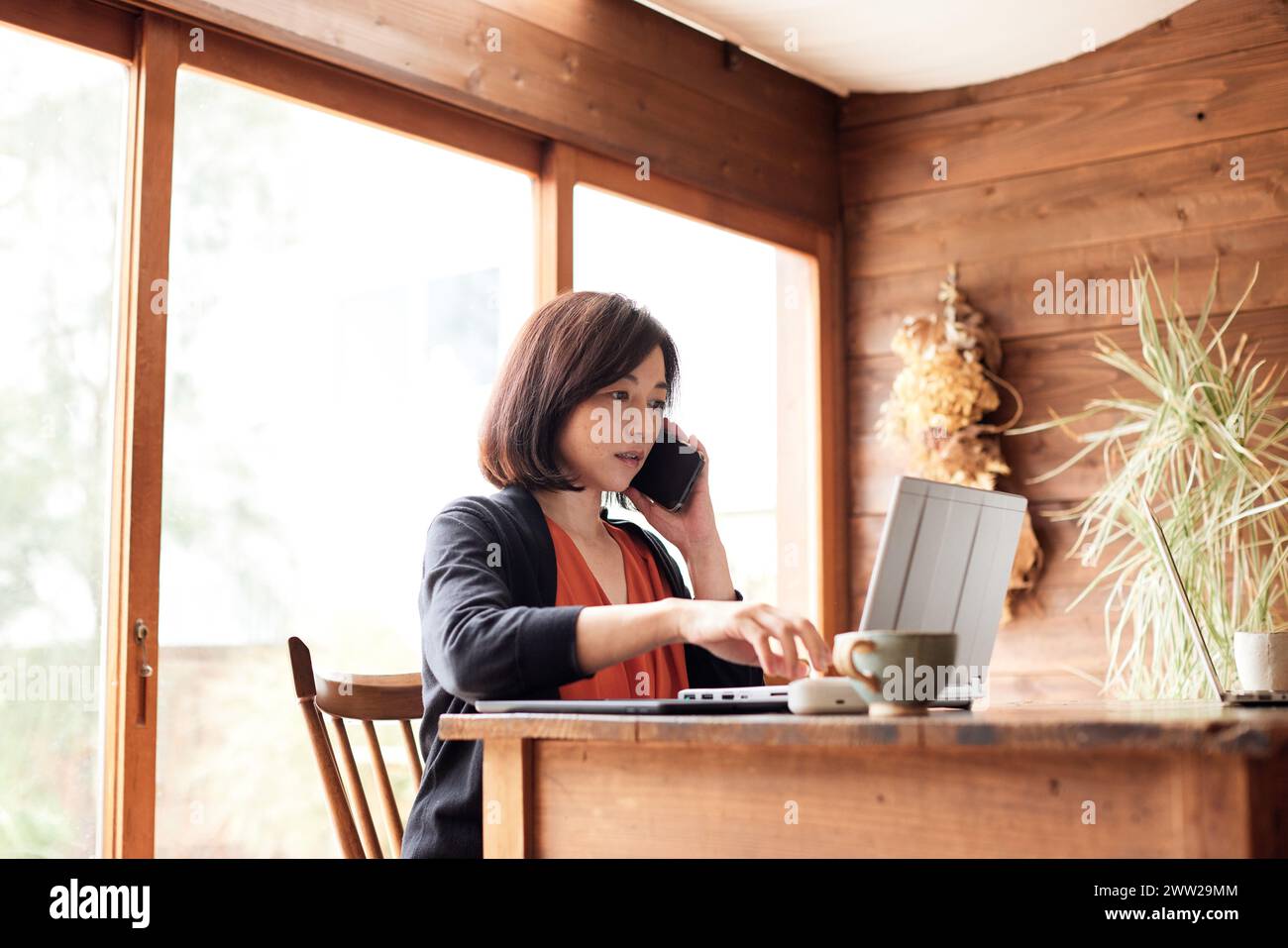 Eine Frau, die an einem Tisch sitzt, mit Laptop und Handy Stockfoto