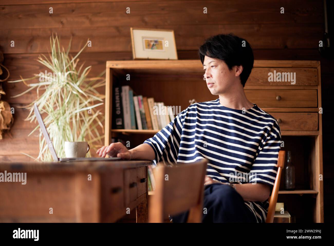 Ein Mann in gestreiftem Hemd, der mit einem Laptop an einem Schreibtisch sitzt Stockfoto