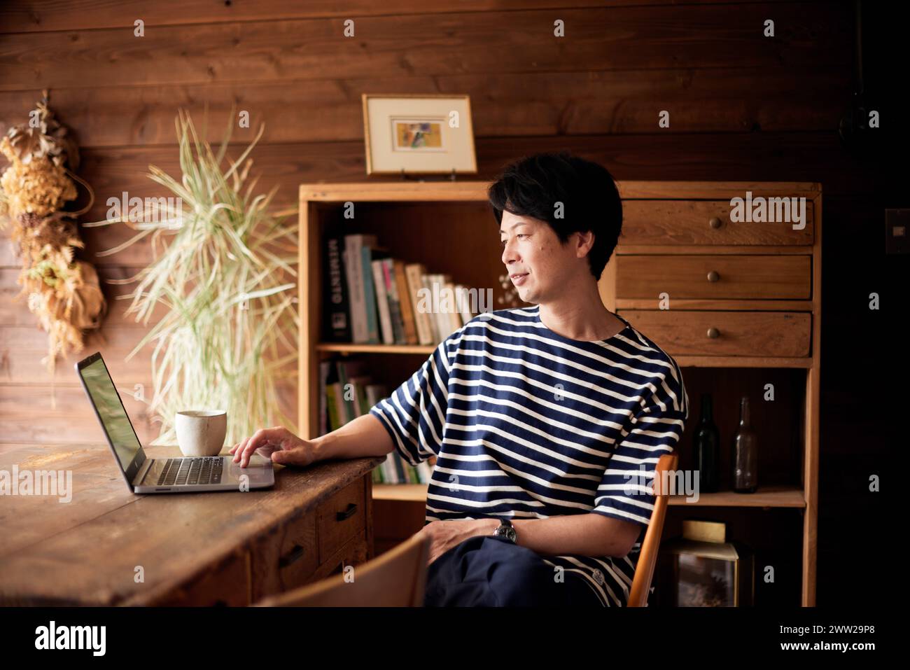 Ein Mann in gestreiftem Hemd, der an einem Schreibtisch mit Laptop sitzt Stockfoto
