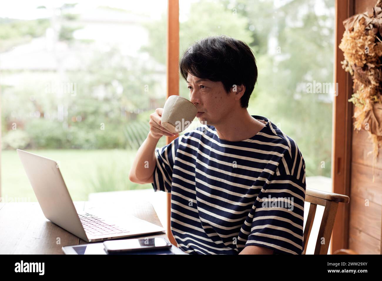 Ein Mann in einem gestreiften Hemd, der Kaffee trinkt, während er an seinem Laptop arbeitet Stockfoto