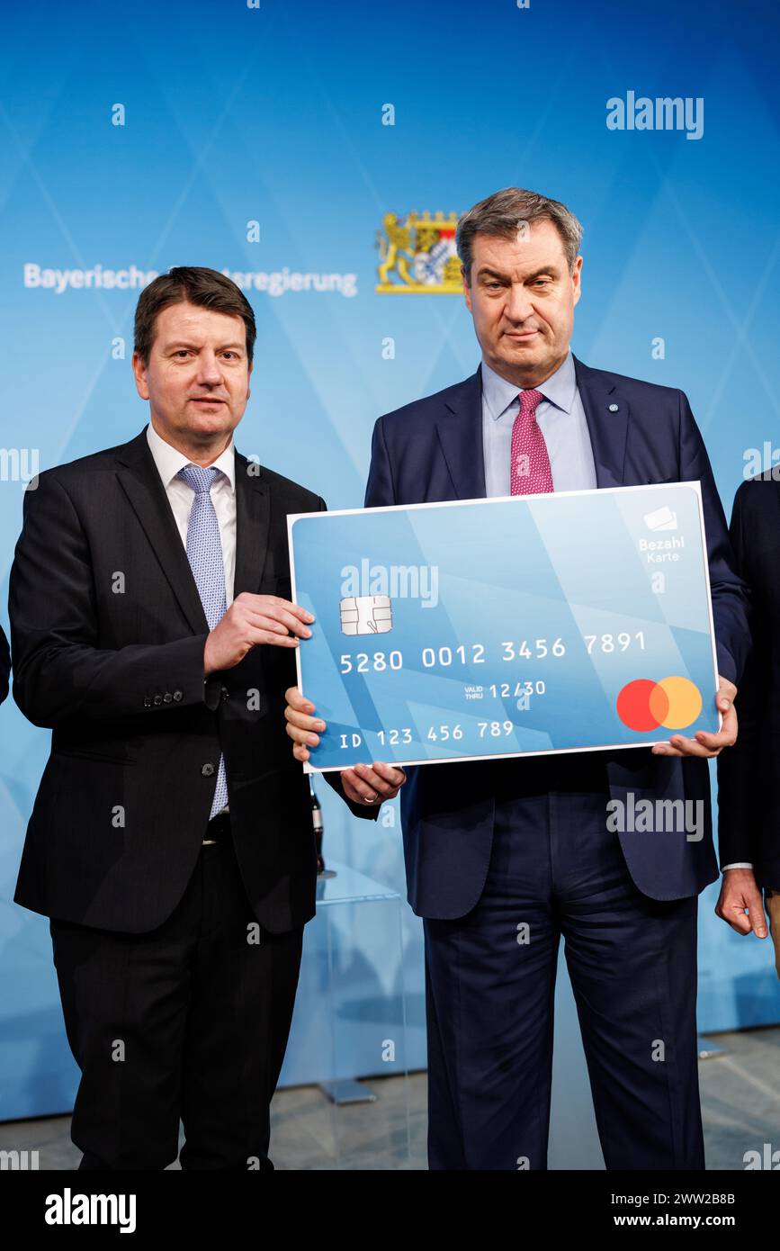 20. März 2024, Bayern, München: Markus Söder (CSU), Parteivorsitzender und Ministerpräsident Bayerns, und Sandro Kirchner (CSU), Staatssekretär im Bayerischen Innenministerium, zeigen auf der Pressekonferenz zur Präsentation der bayerischen Zahlungskarte für Asylbewerber im Prinz-Carl-Palais am 20. März 2024 ein überdimensionales Modell der Karte vor die Kamera. Nach erfolgreichem Abschluss des Vergabeverfahrens wird in vier Pilotgemeinden, den Landkreisen Fürstenfeldbruck, Günzburg und Traunstein sowie dem Landkreis die Testphase der bayerischen Zahlungskarte für Asylbewerber beginnen Stockfoto