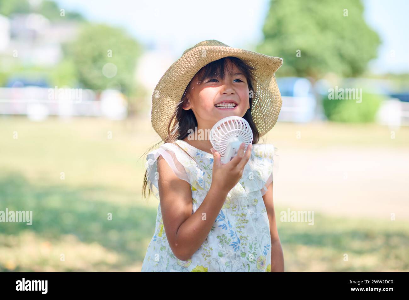 Ein junges Mädchen mit einem Hut, der einen weißen Ventilator hält Stockfoto