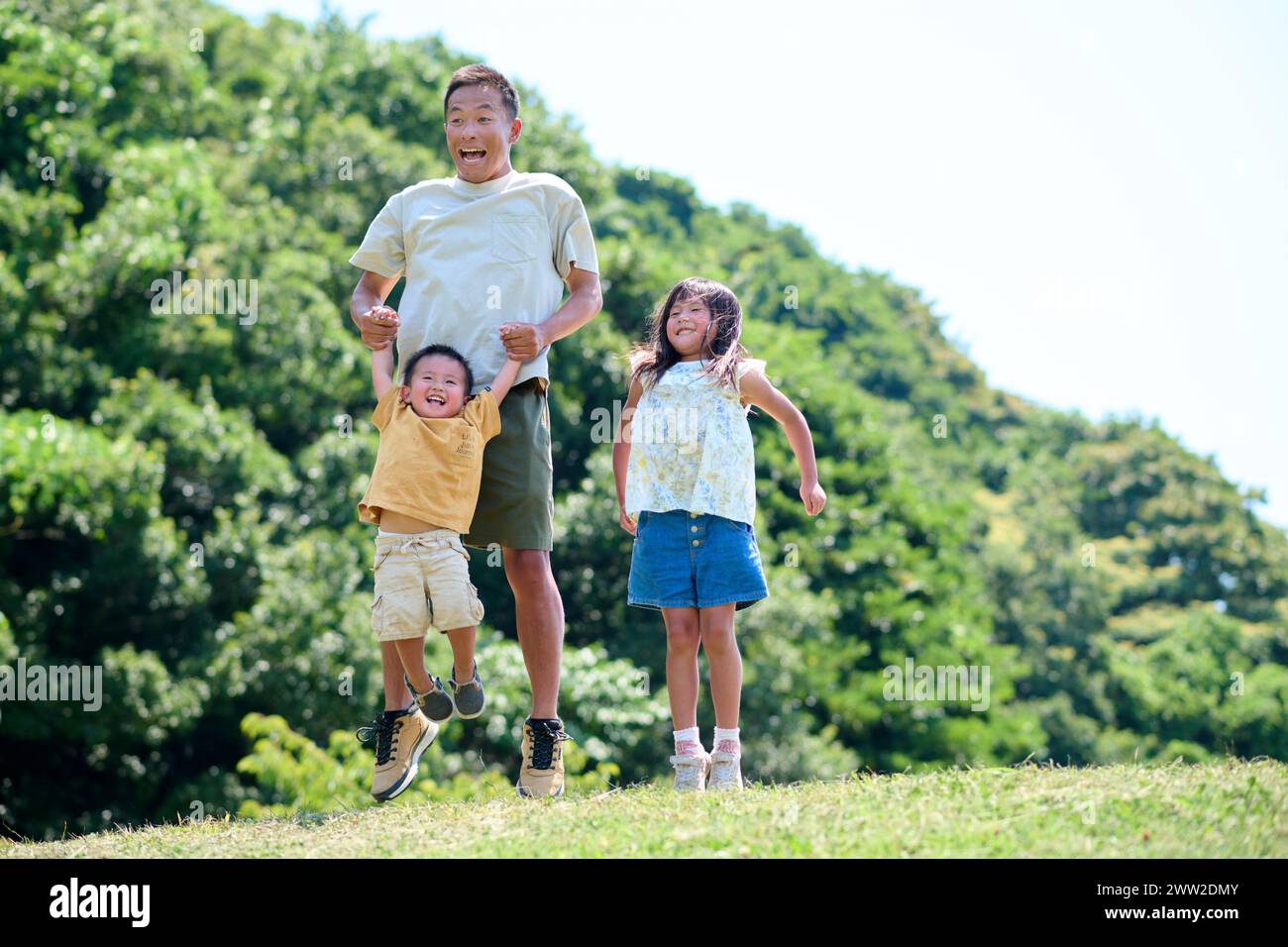 Ein Mann und zwei Kinder, die auf das Gras springen Stockfoto