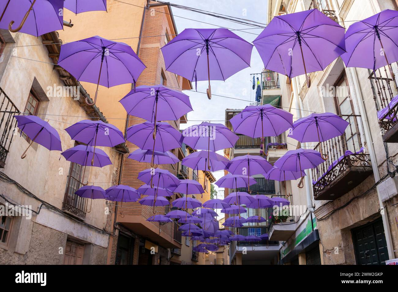 Viele violette Regenschirme hängen mitten auf der Straße, die den Touristen, die Brihuega besuchen, Schatten spenden Stockfoto