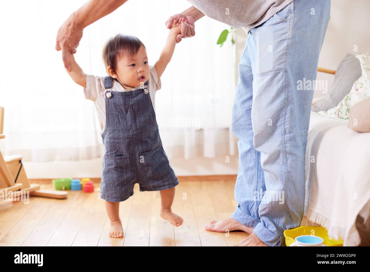 Ein Mann, der die Hand eines Kleinkindes hält, während er auf einem Holzboden steht Stockfoto