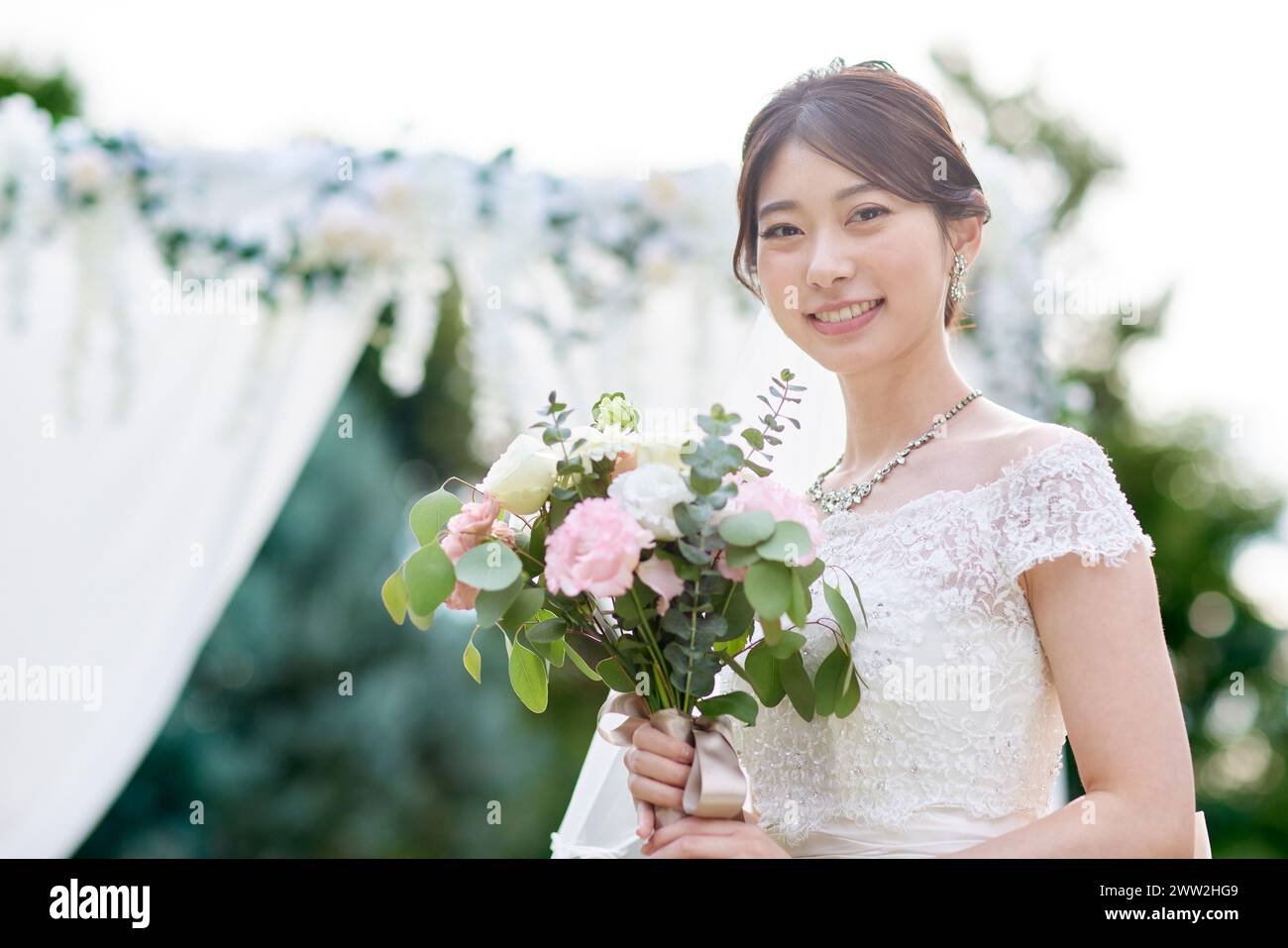 Asiatische Braut mit Blumenstrauß vor dem Hochzeitsbogen Stockfoto