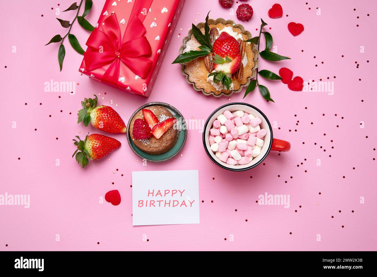 Festlicher rosafarbener Hintergrund mit Cupcake, Erdbeeren, Schokolade, heißem Getränk. Geburtstagsfeier. Draufsicht Stockfoto