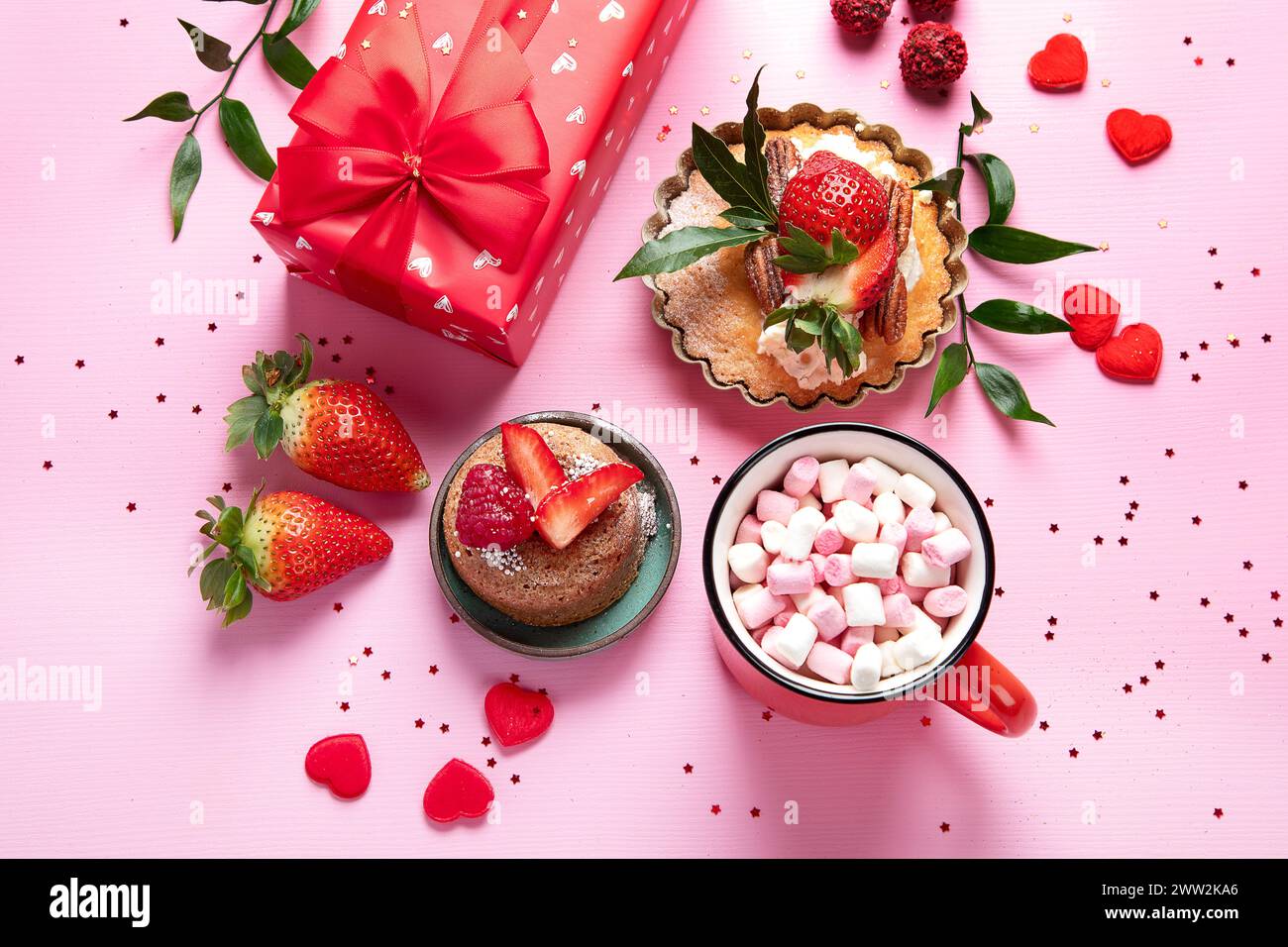 Festlicher rosafarbener Hintergrund mit Cupcake, Erdbeeren, Schokolade, heißem Getränk. Geburtstagsfeier. Draufsicht Stockfoto