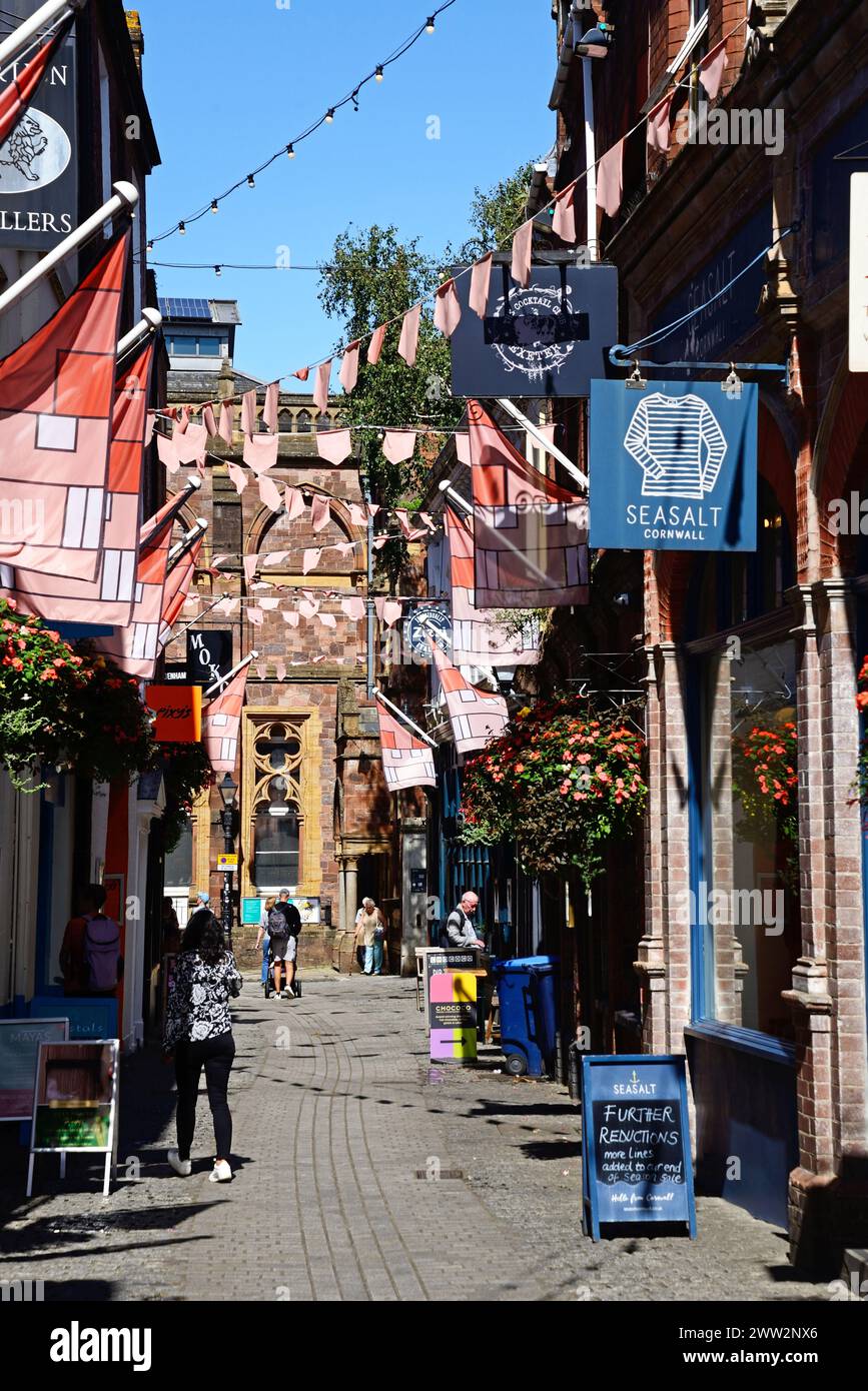 Menschen gehen entlang der Gandy Street, gesäumt von Geschäften und Restaurants, mit einem Teil des Royal Albert Memorial Museums und der Kunstgalerie nach hinten, Exeter, Großbritannien. Stockfoto