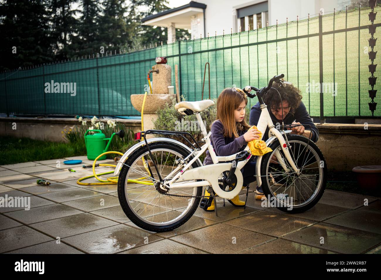Kaukasischer Vater und Schulmädchen-Tochter im Garten putzen ihr Fahrrad für den Frühling. Stockfoto