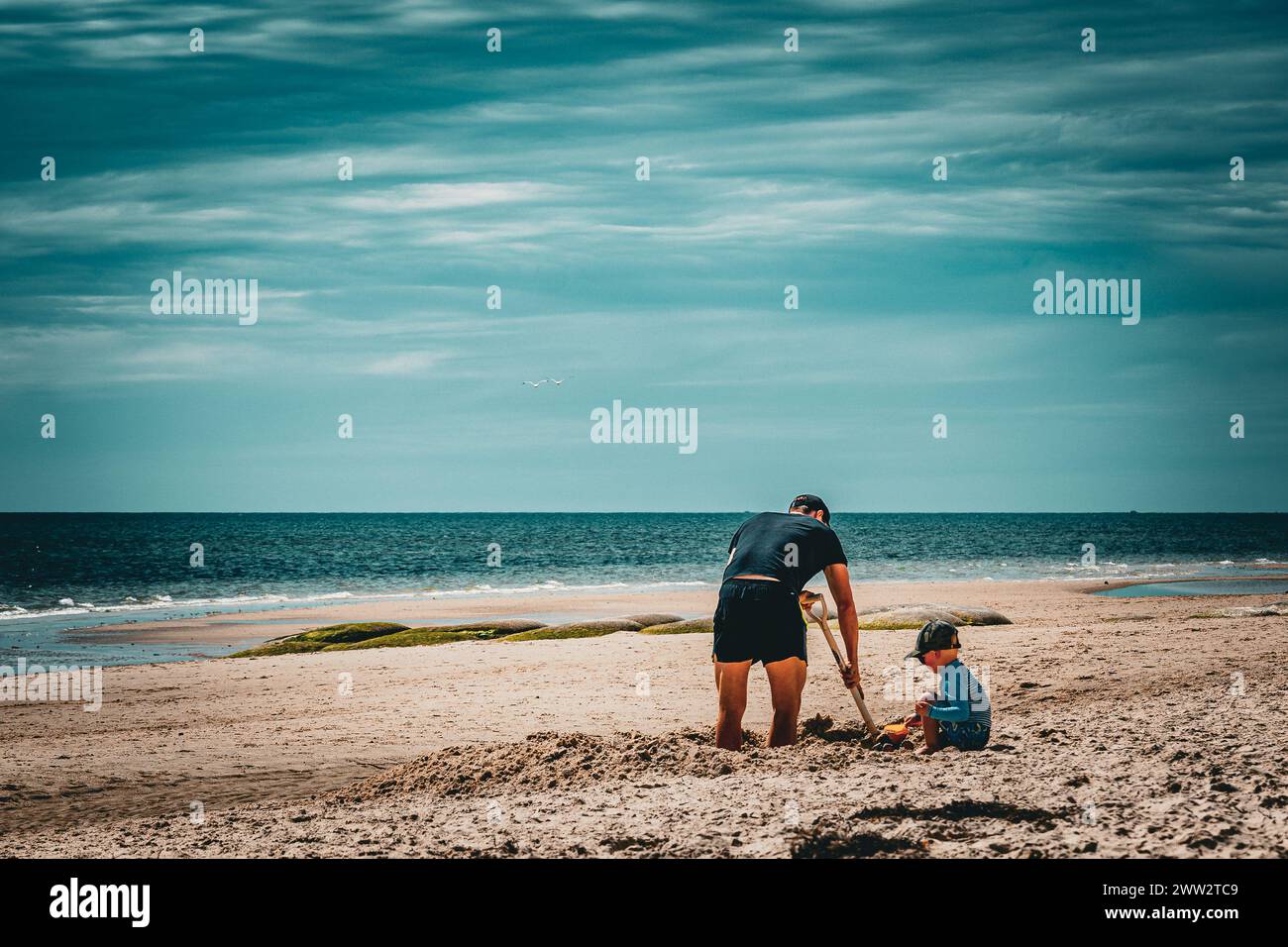 Ein Erwachsener und ein Kind graben gemeinsam im Sand an einem sonnigen Strand. Stockfoto