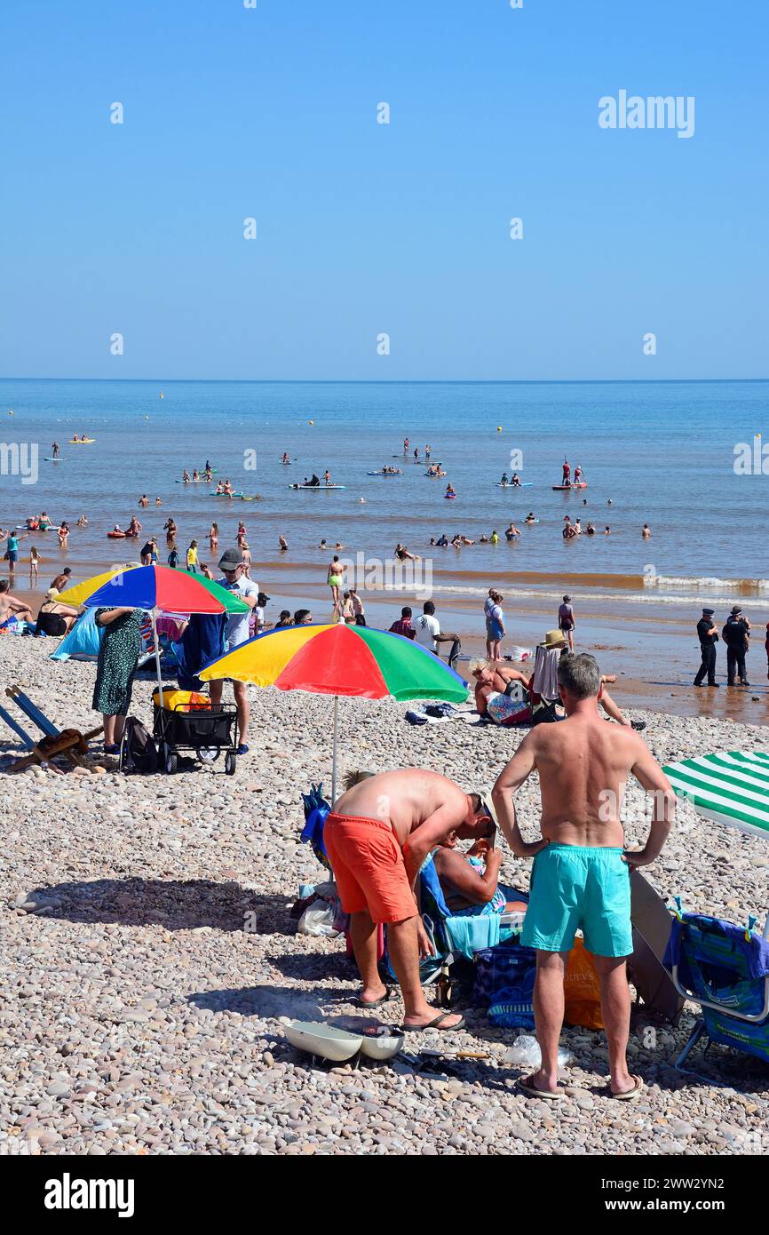 Touristen entspannen am Strand mit Polizeiangeboten auf der rechten Seite und Blick auf das Meer, Sidmouth, Devon, Großbritannien, Europa. Stockfoto