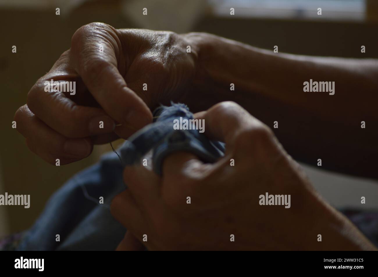 Manos de mujer cosiendo una prenda de ropa, en la fotografía se puede apreciar el hilo y la tela. Stockfoto