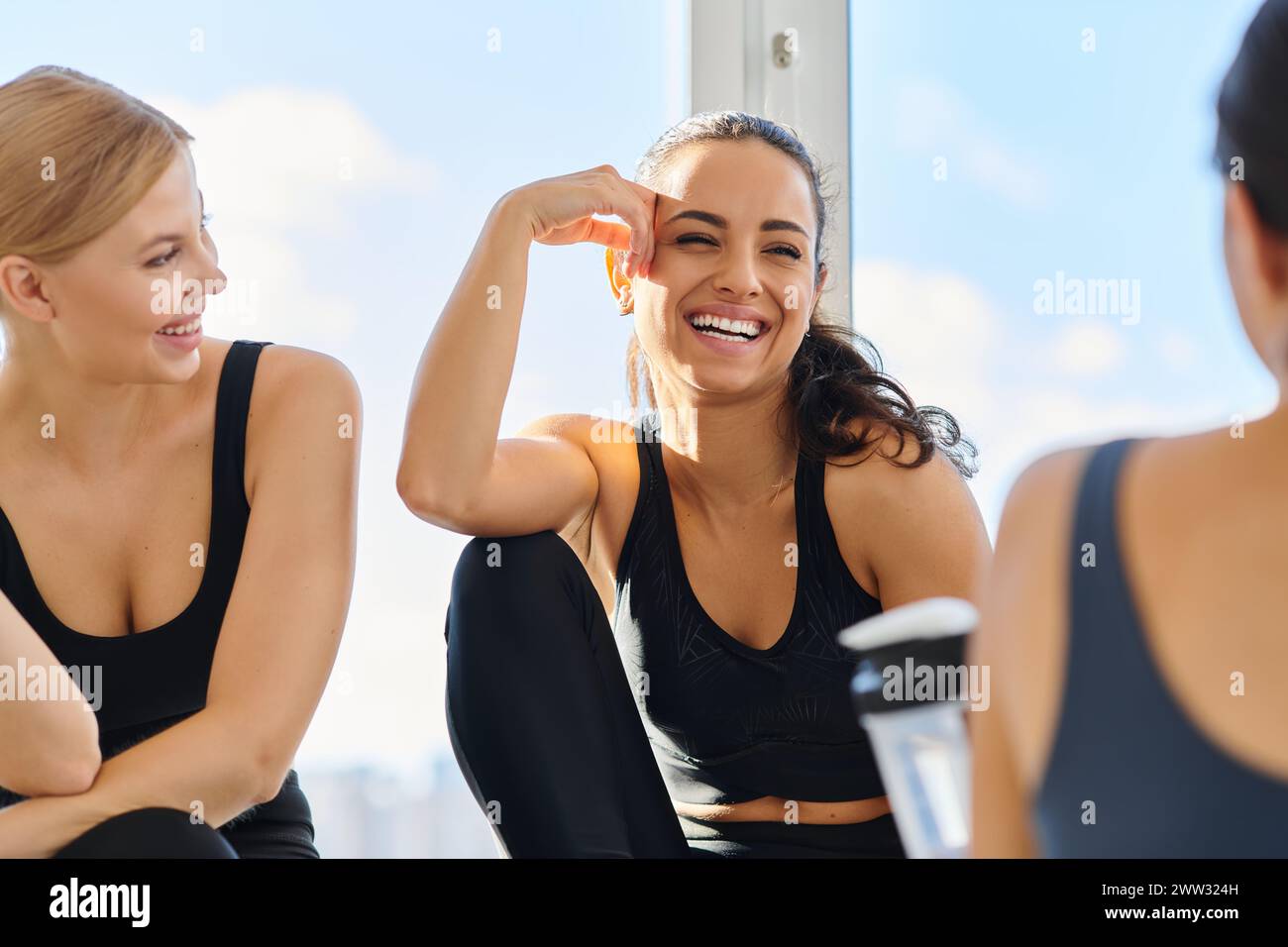 Sonnenlicht auf dem Gesicht einer fröhlichen brünetten Frau in aktiver Kleidung lacht nach dem Workout mit ihren Freunden Stockfoto