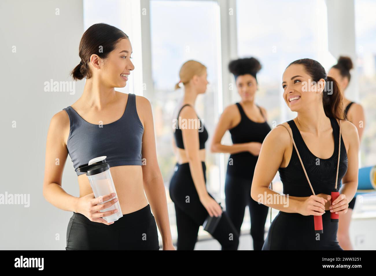 Fröhliche multikulturelle Freundinnen in aktiver Kleidung, die sich nach dem Pilates-Workout anlächeln Stockfoto
