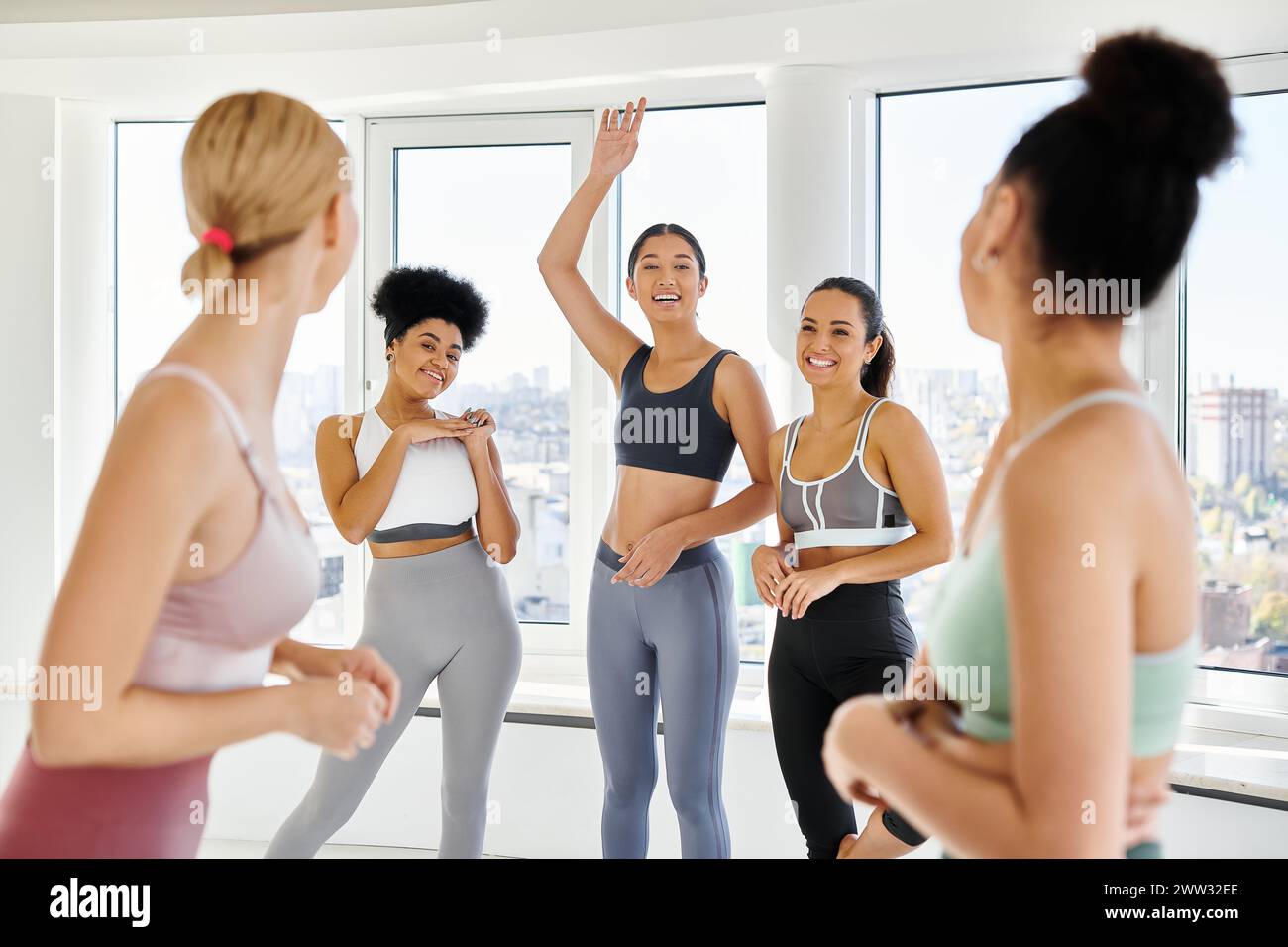 Konzentriere dich auf asiatische Frauen in Sportbekleidung, die ihren weiblichen Freunden im Pilates-Kurs zuwinken, eine vielfältige Gruppe Stockfoto