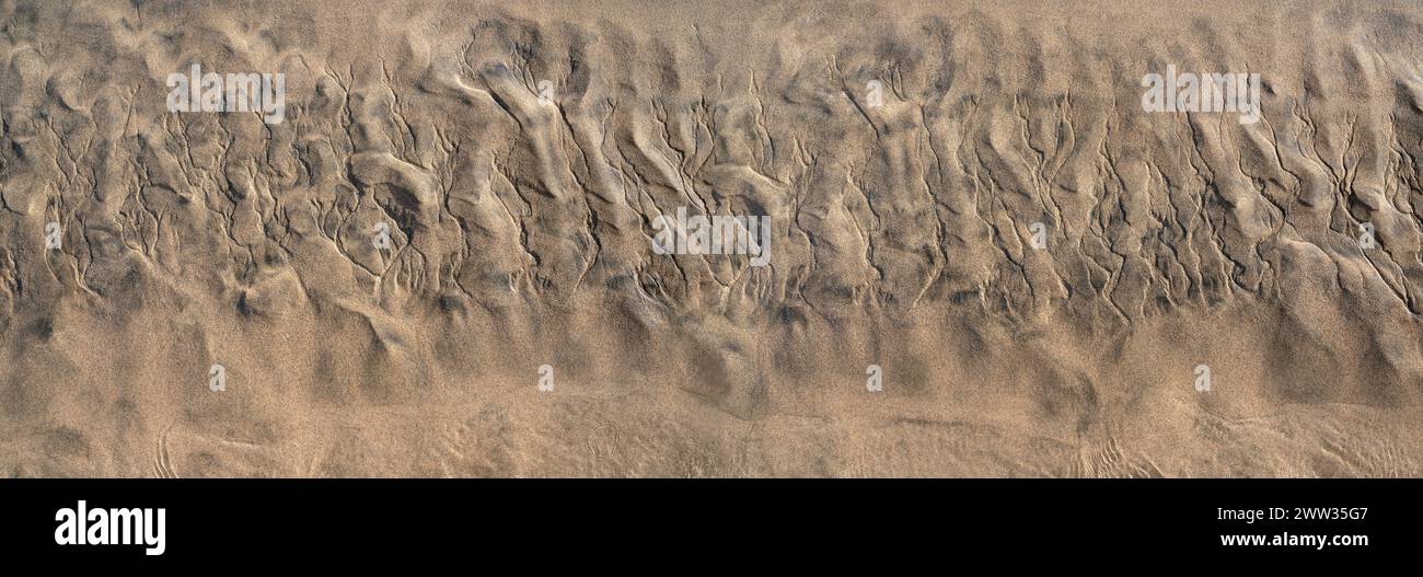 Abstrakte Struktur im braunen Sand am Strand bei Ebbe, unten mit flachem Wasser Stockfoto