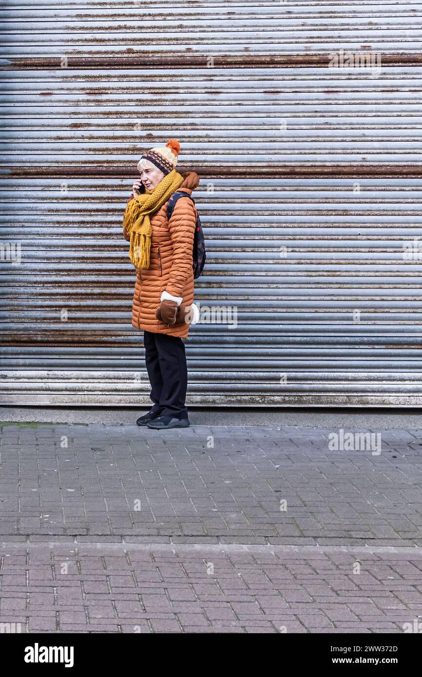Eine reife Frau, die auf ihrem Handy spricht, steht vor einem verschlossenen Ladenladen im Stadtzentrum von Newquay in Cornwall, Großbritannien. Stockfoto