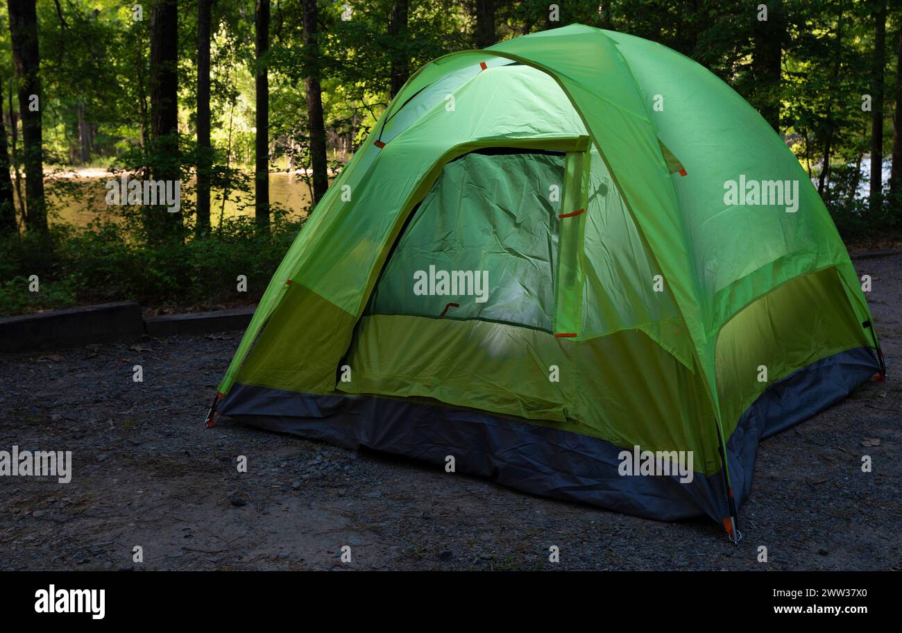 Zwei Männer, die ein Zelt auf einem Campingplatz mit Lichtern im Inneren und einem See im Sonnenlicht dahinter haben. Stockfoto