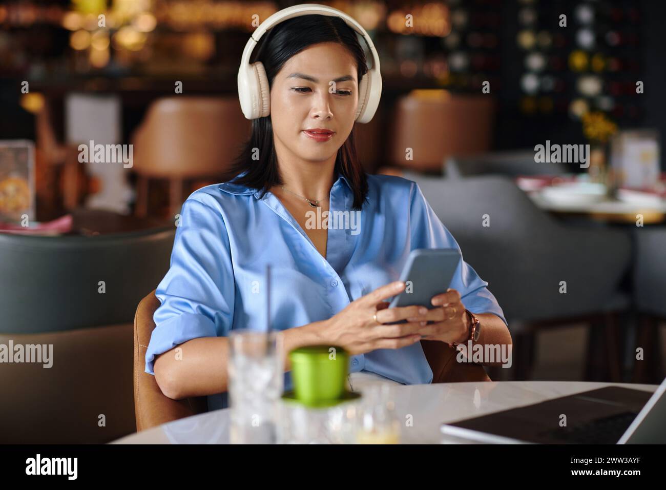 Frau im Kopfhörer sitzt am Restauranttisch und hört Musik auf dem Smartphone Stockfoto