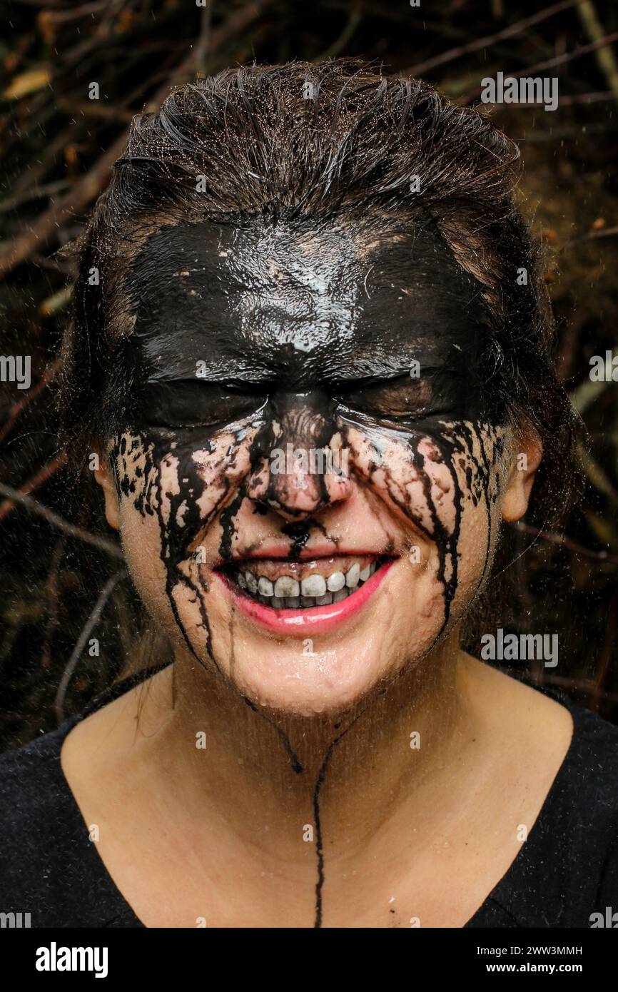 Ein fröhliches Lächeln bricht durch eine komplizierte Maske aus schwarzer Farbe, inmitten eines natürlichen, zwielichtigen Hintergrunds. Stockfoto