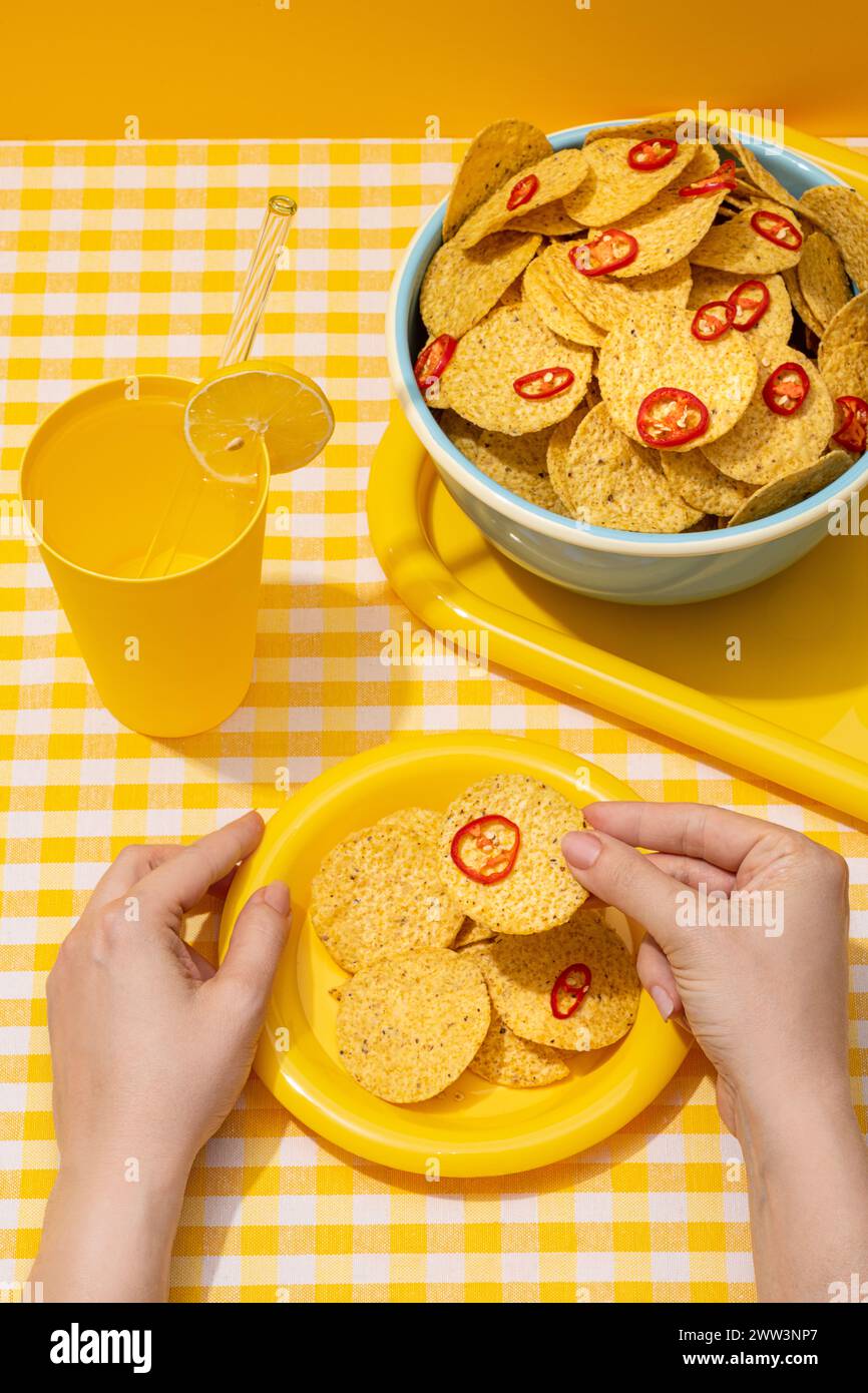 Runde Nachos-Maistortilla-Chips mit roten Chilischeiben in einer Snackschale mit einem kalten Getränk Stockfoto