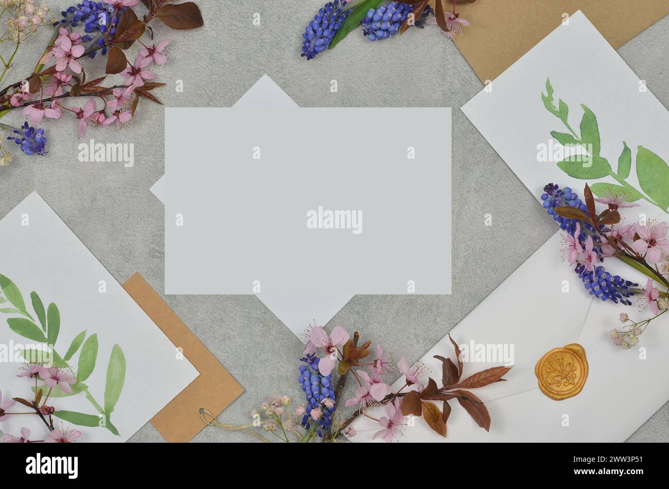 Komposition auf einem Tisch mit kleinen Blumen, Umschlägen, weißen Blättern und bemalten Blättern mit leerem Platz zum Ausfüllen des Inhalts. Stockfoto