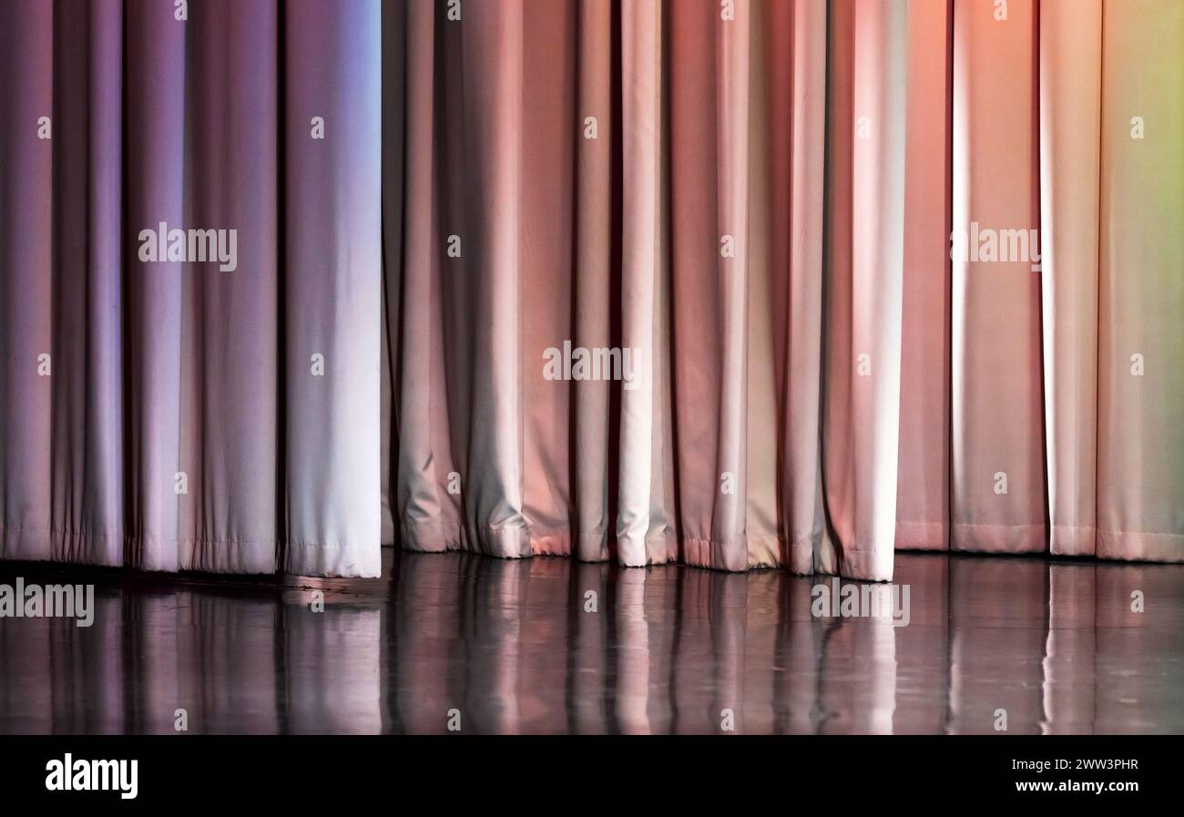 Geschlossener weißer wellenförmiger Vorhang unter farbenfroher Beleuchtung hängt über einer leeren Bühne, Hintergrundfotostruktur Stockfoto
