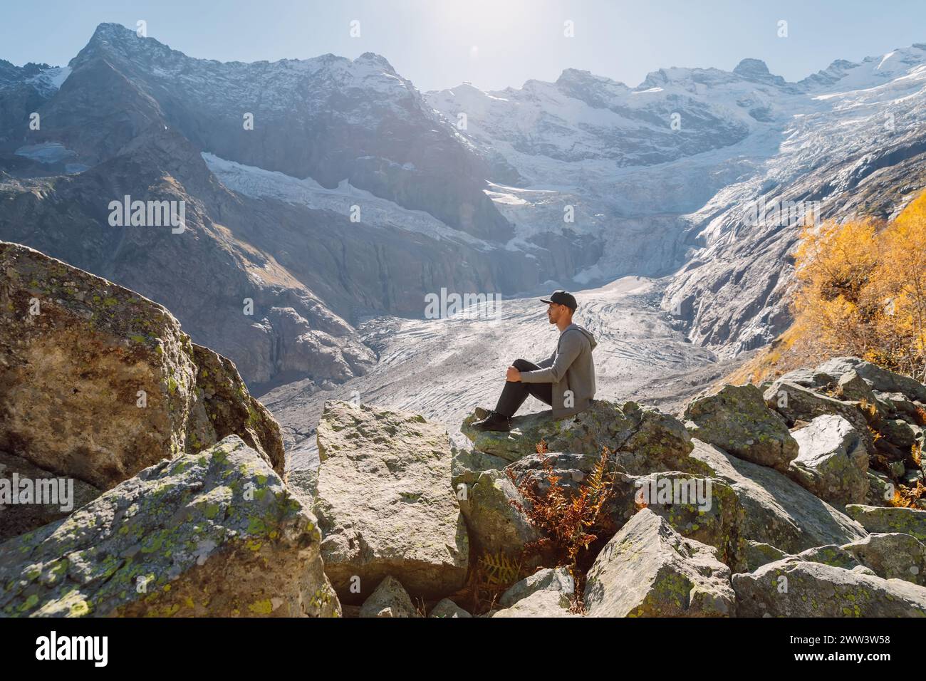 Ein Mann, der sich entspannt und auf dem Felsen in den höchsten Bergen sitzt. Berg mit Gletscher und Touristen Stockfoto