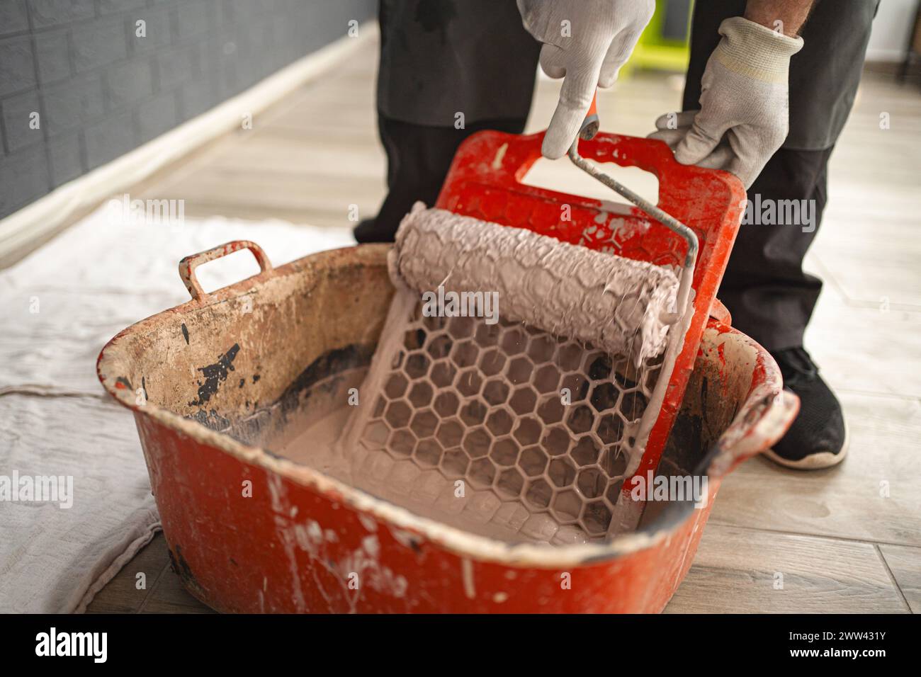 Man taucht eine Malerwalze ein, um überschüssige Farbe auf dem Abzieher abzuwischen Stockfoto