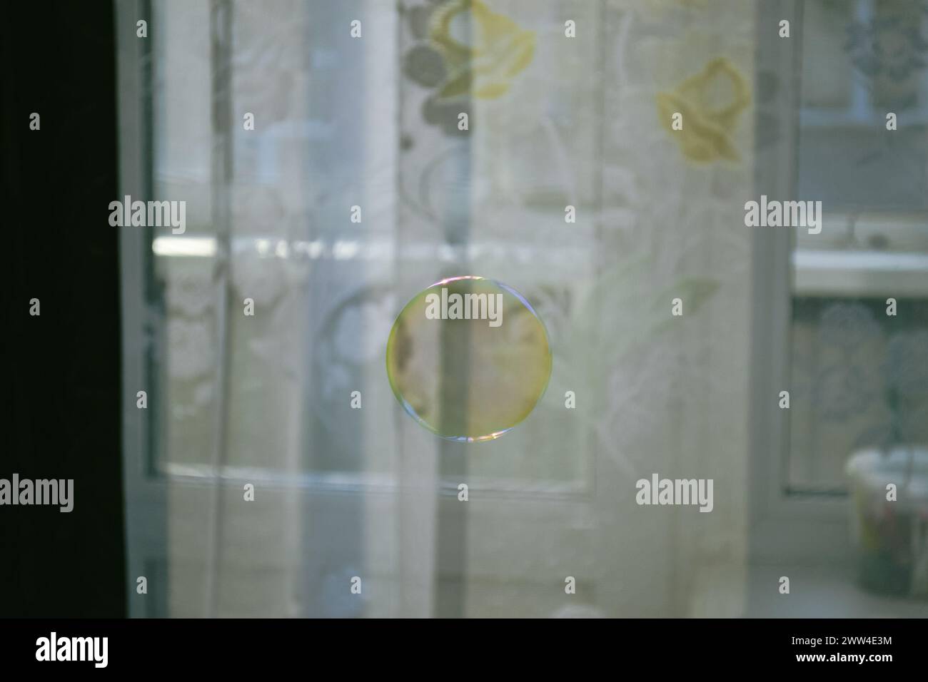 Perfekt runde transparente Seifenblase vor dem Hintergrund weißer Vorhänge mit Muster Stockfoto