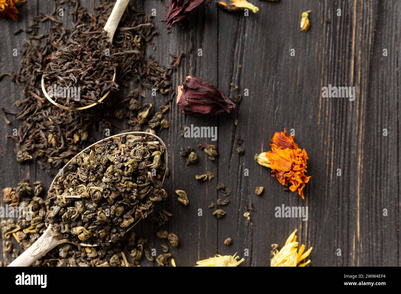 Zusammensetzung von trockenem schwarzem und grünem Tee in alten Löffeln, trockenem Blumentee auf dunklem Holzhintergrund, Nahaufnahme von oben. Verschiedene Arten von trockenem Tee Stockfoto