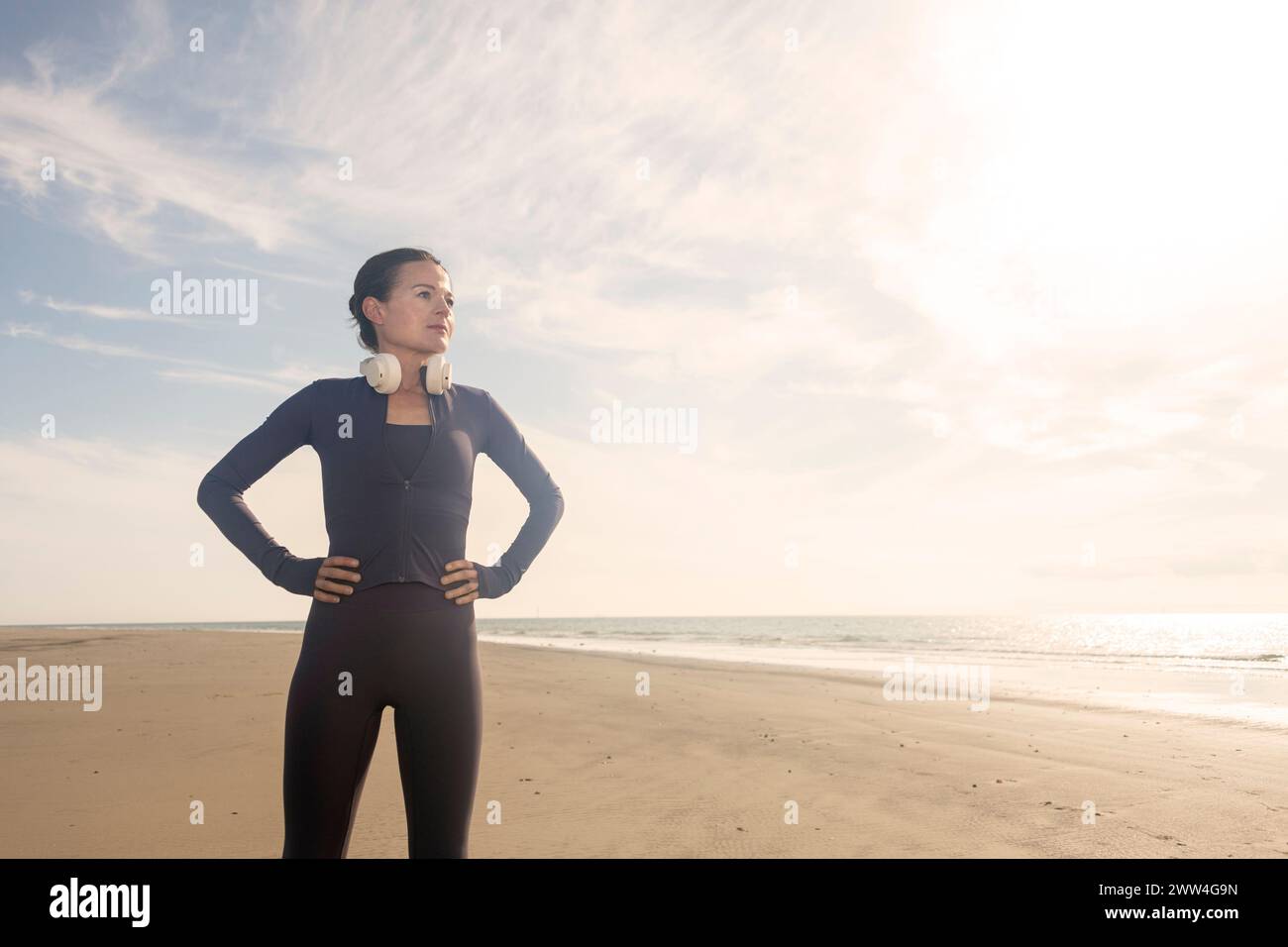 Läuferin am Strand mit Händen auf Hüften vor blauem Himmel Stockfoto