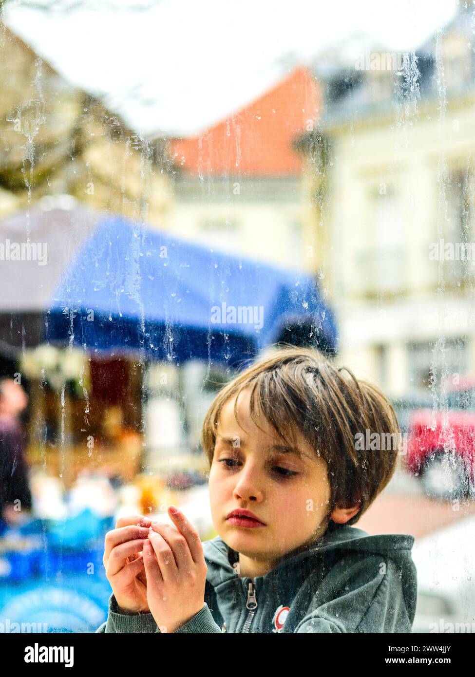 Junger Junge, der durch das regendurchflutete Fenster mit Fingern blickt - Preuilly-sur-Claise, Indre-et-Loire (37), Frankreich. Stockfoto