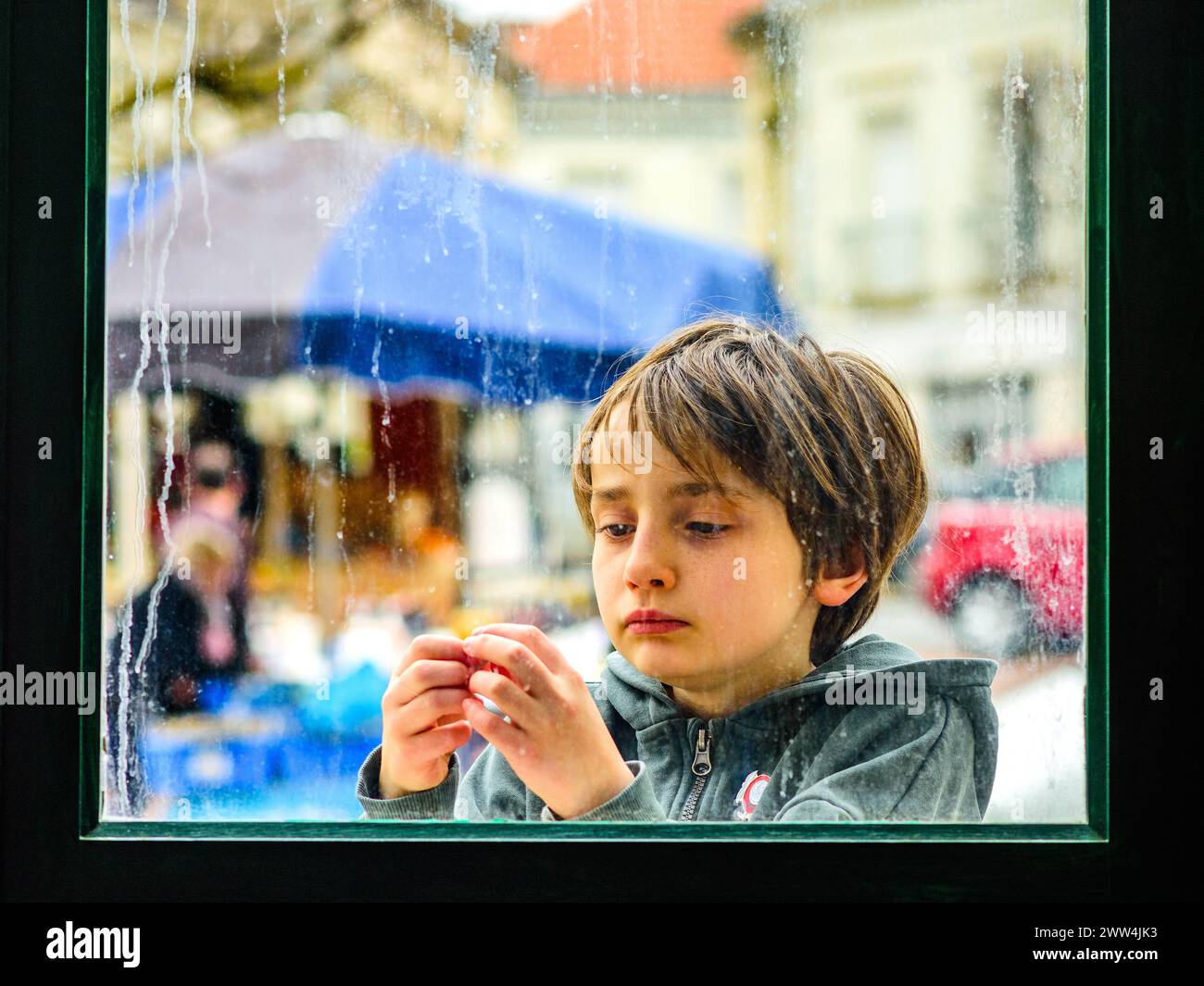 Junger Junge, der durch das regendurchflutete Fenster mit Fingern blickt - Preuilly-sur-Claise, Indre-et-Loire (37), Frankreich. Stockfoto